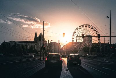 Vehicles on road against sky during sunset