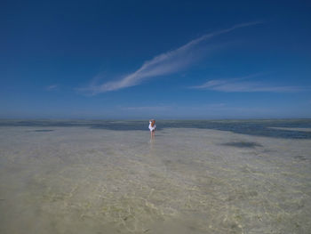 Rear view of woman standing on beach against sky