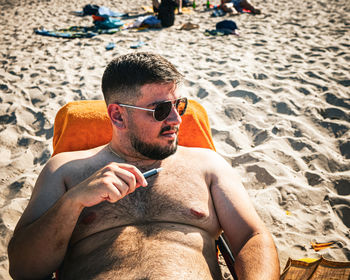 Portrait of young man sitting on sand at beach