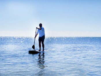 Full length of man paddleboarding in sea against sky