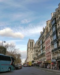 Cars on city street by buildings against sky