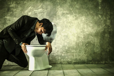 Young man feeling sick on toilet against wall