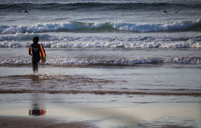 Rear view of man walking at beach with surfboard