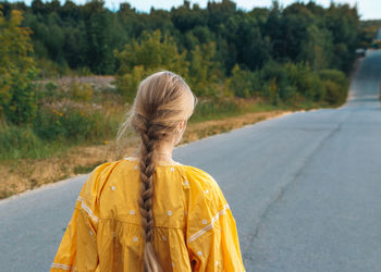 Rear view of woman with long braid standing on road against trees