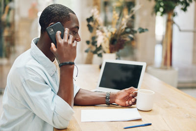 Young woman using mobile phone while sitting on table