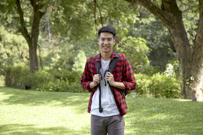 Smiling young man standing against trees
