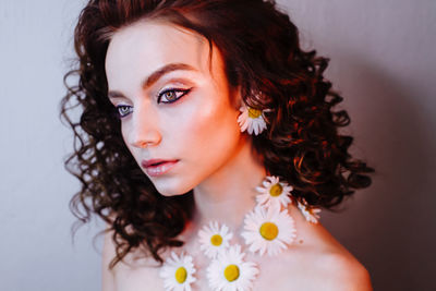 Close-up of beautiful young woman wearing flowers and make-up against wall