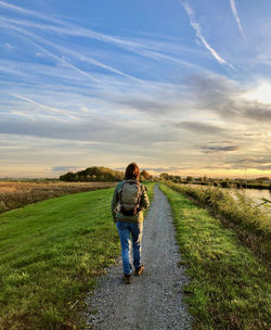 Rear view of a woman walking over a green dike in the morning sun