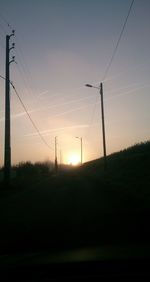 Electricity pylon on field against sky at sunset