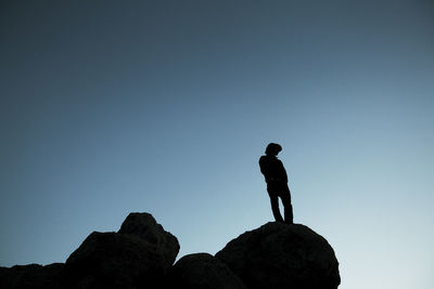 Low angle view of silhouette man standing on rock against clear blue sky at dusk