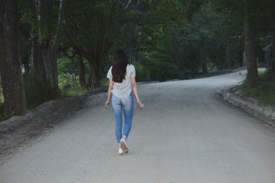 Rear view of woman walking on road amidst trees in forest