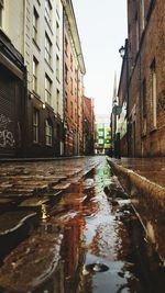 Wet street amidst buildings in city