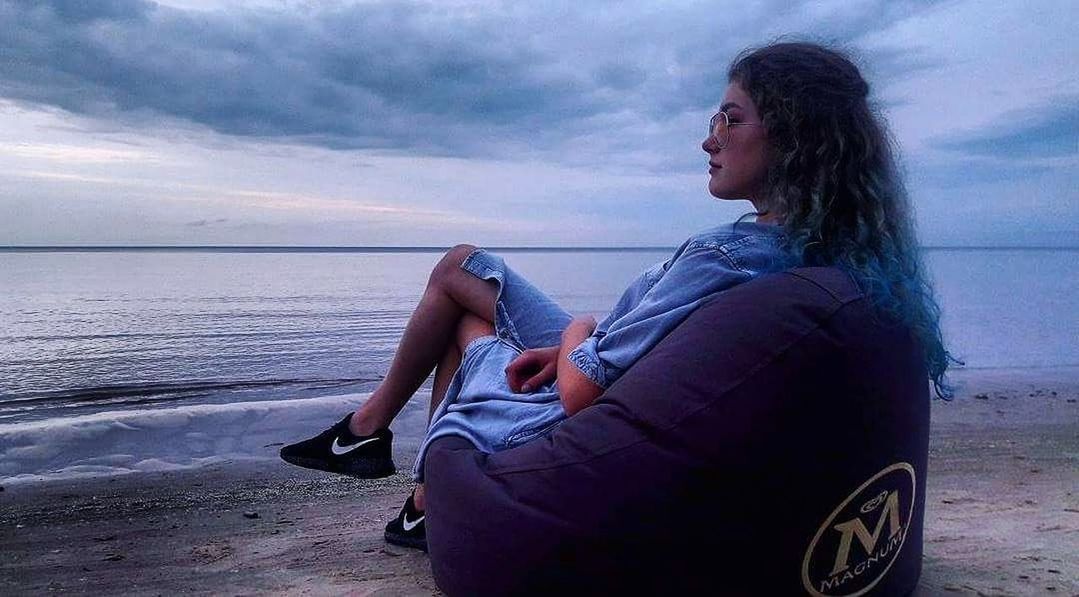 WOMAN SITTING ON BEACH AGAINST SEA