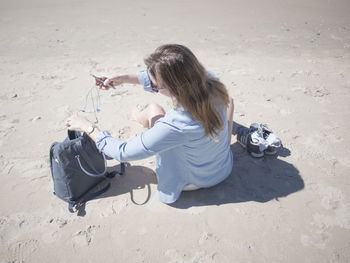 High angle view of woman with mobile phone while taking earphones out of bag at beach