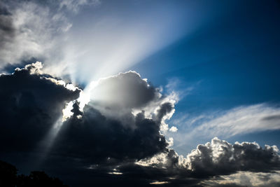 Low angle view of sunlight streaming through clouds