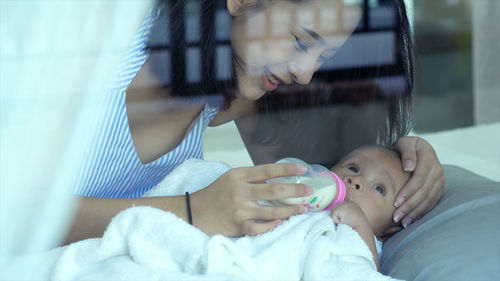 Mother feeding milk to cute baby son seen through glass window