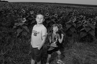 Siblings standing on flower field against clear sky during sunset