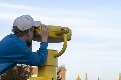 Boy is looking into big iron binocular on mountain viewpoint. travelling in beautiful places.