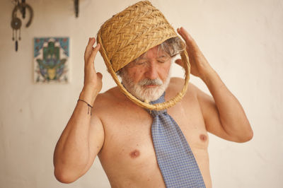 Portrait of shirtless man wearing hat standing against wall