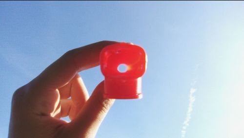 Close-up of hand holding red toy against blue sky