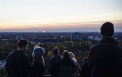 Rear view of people in city against sky during sunset