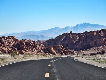 Empty road leading towards mountains against blue sky