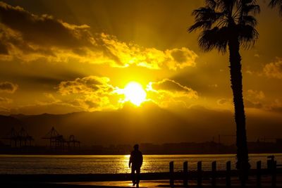 Silhouette woman by sea against sky during sunset