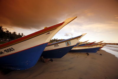 Boats moored at beach against cloudy sky during sunset