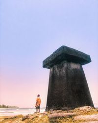 Rear view of man standing on rock against sky