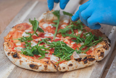Hands with plastic gloves adding fresh rocket leaves on a pizza with tomato sauce and mozzarella