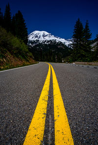 Surface level of road amidst trees and mountains against blue sky
