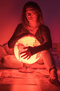 Mid adult woman sitting on illuminated wall at night