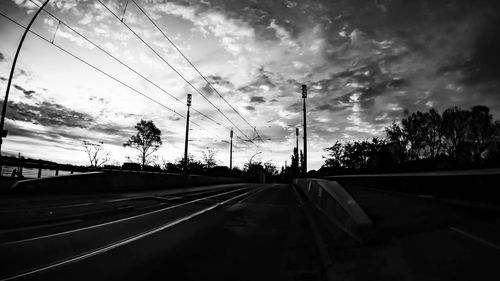 Road by railroad tracks against sky during sunset