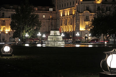 Illuminated street by buildings in city at night