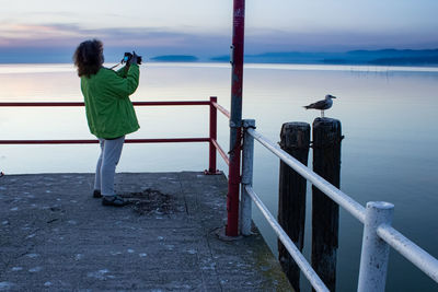 Full length of woman photographing lake while standing on pier