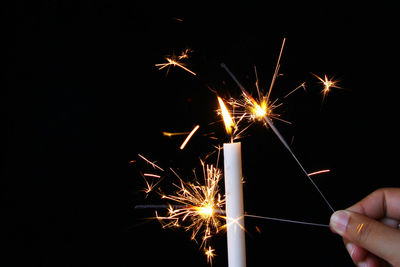 Cropped hand holding sparklers against black background