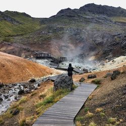 Rear view of woman walking on boardwalk by hot spring