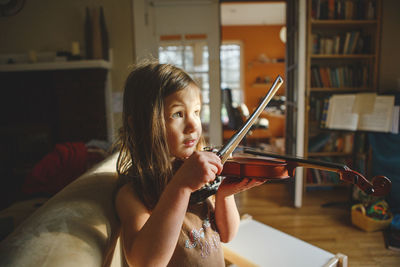 Close-up of girl playing violin while sitting on sofa at home