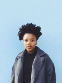 Portrait of young woman wearing overcoat standing against wall