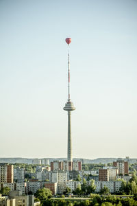 Communications tower and hot air balloon amidst buildings in city against sky