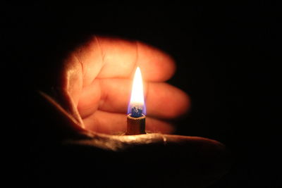 Close-up of hand holding illuminated candle in darkroom