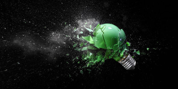 Green electric light bulb exploding on black.