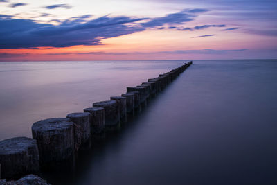 Wooden posts in sea against sky during sunset