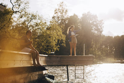 Smiling mature couple talking while looking away at patio by lake during sunny day