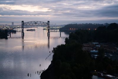 Bridge over river in city against sky during sunset