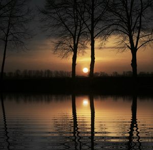 Silhouette trees by lake against sky during sunset