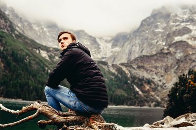 Young woman sitting on rock against mountains