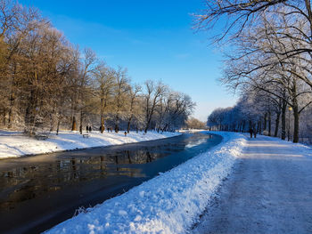 Snow covered trees by canal against sky