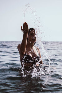 Woman splashing water in sea against clear sky