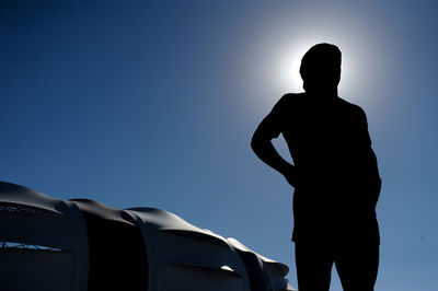 Low angle view of silhouette man standing against airplane against clear blue sky